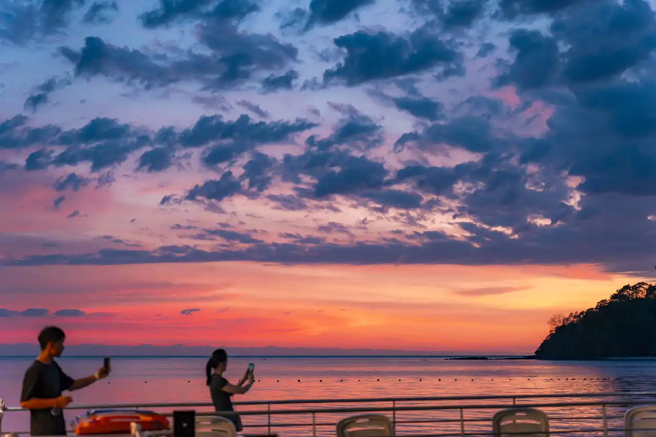 Sunset over a beach with people capturing the view on their phones.